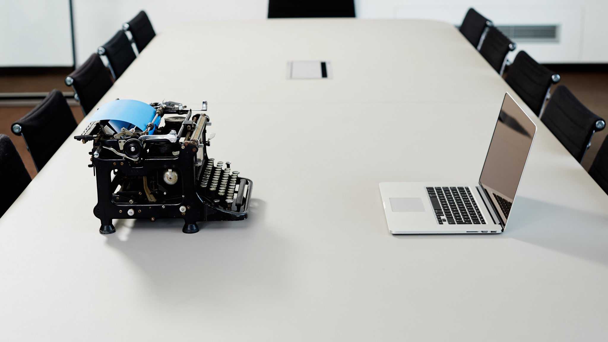 Modernes Notebook steht einer alten Schreibmaschine auf einem Konferenztisch gegenüber